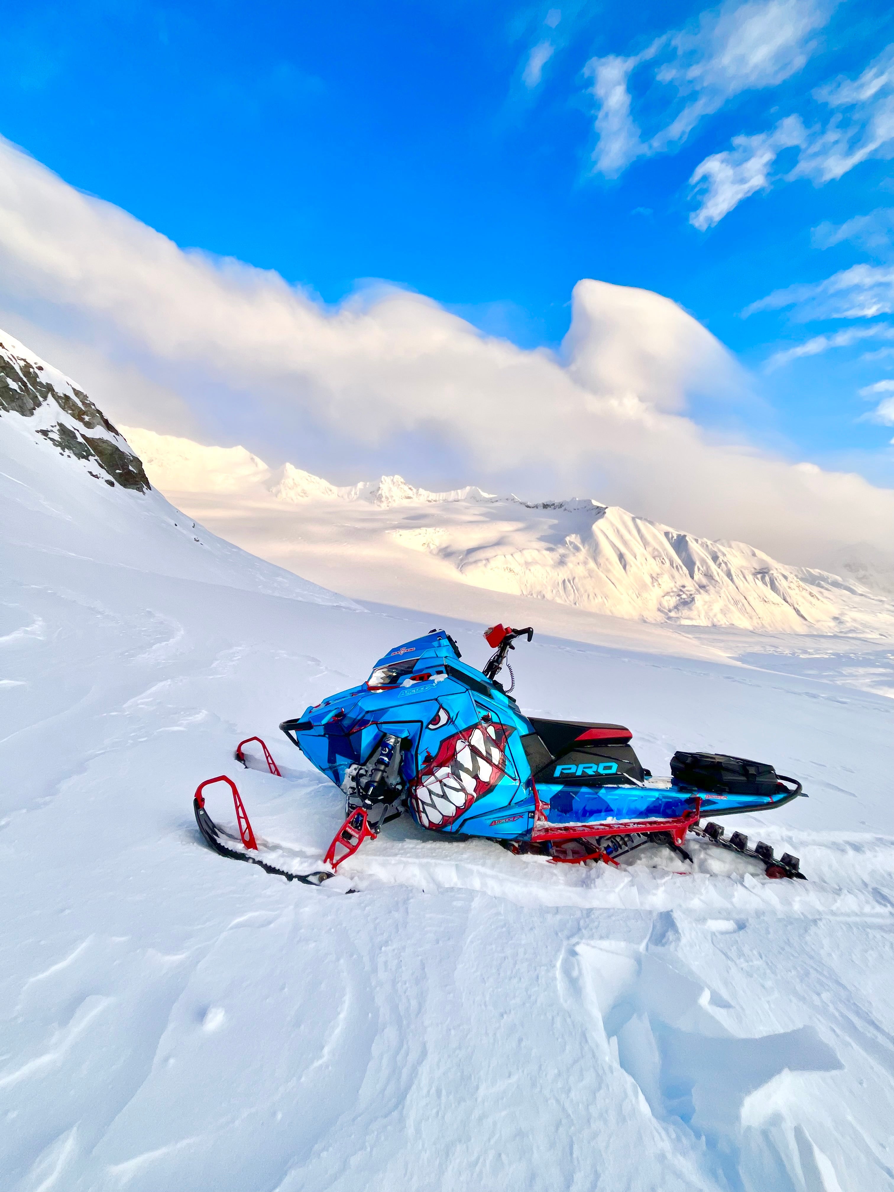 Blue and red snowmobile on a snowy landscape with mountains in the background