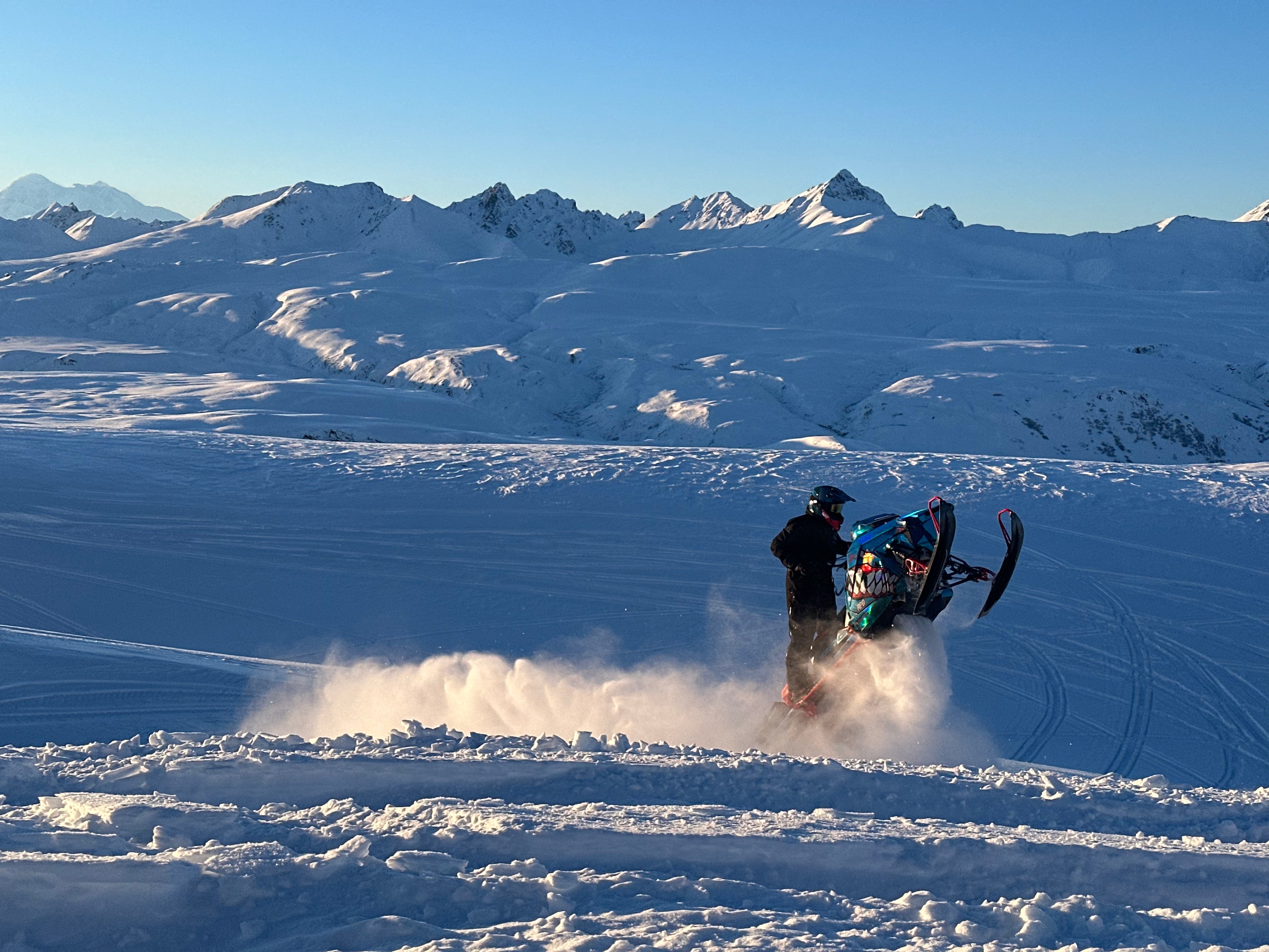 Person on a snowmobile in a snowy landscape with mountains in the background wheelie through life