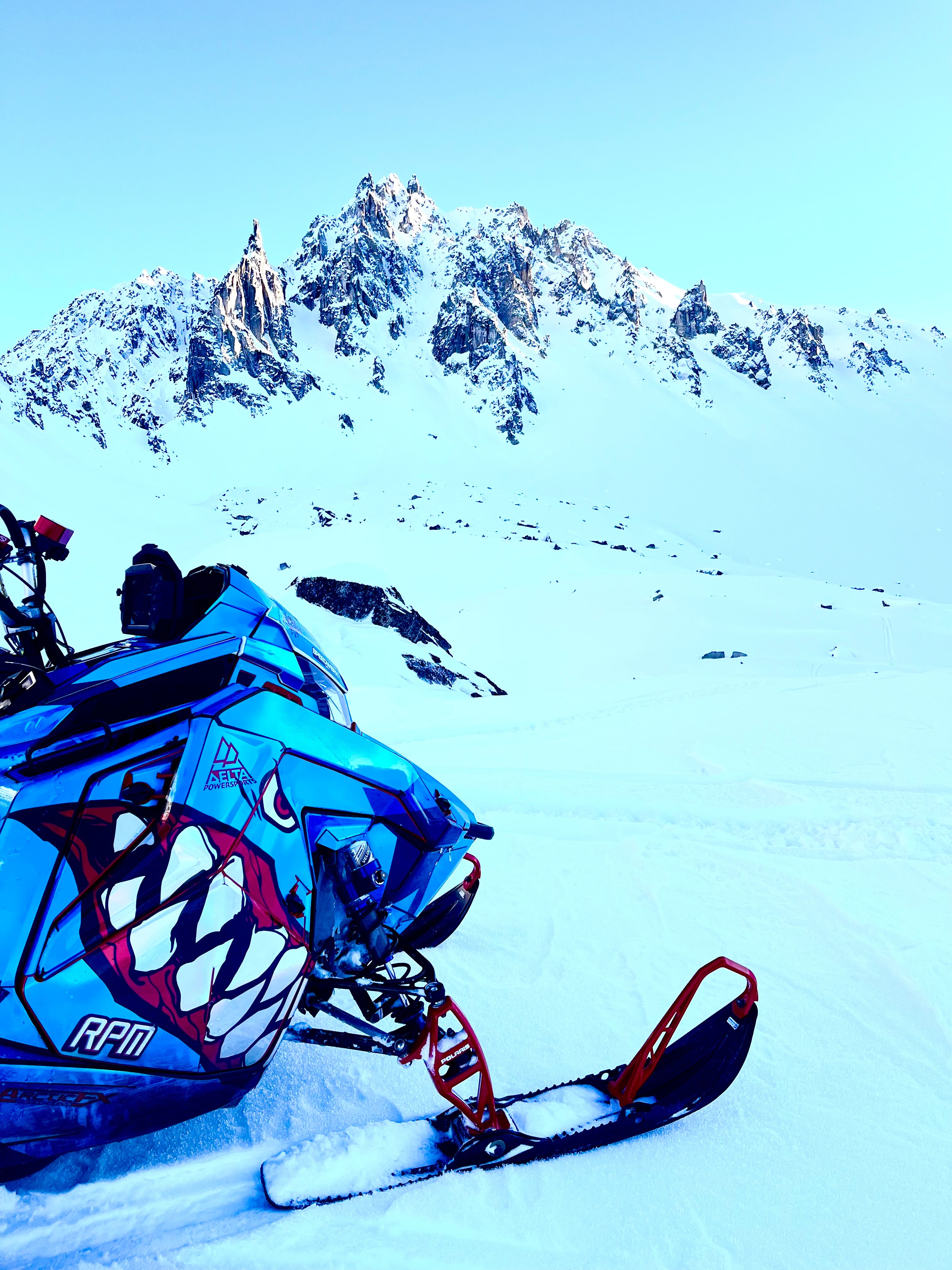 Blue snowmobile with shark mouth in the snow with a mountain in the background