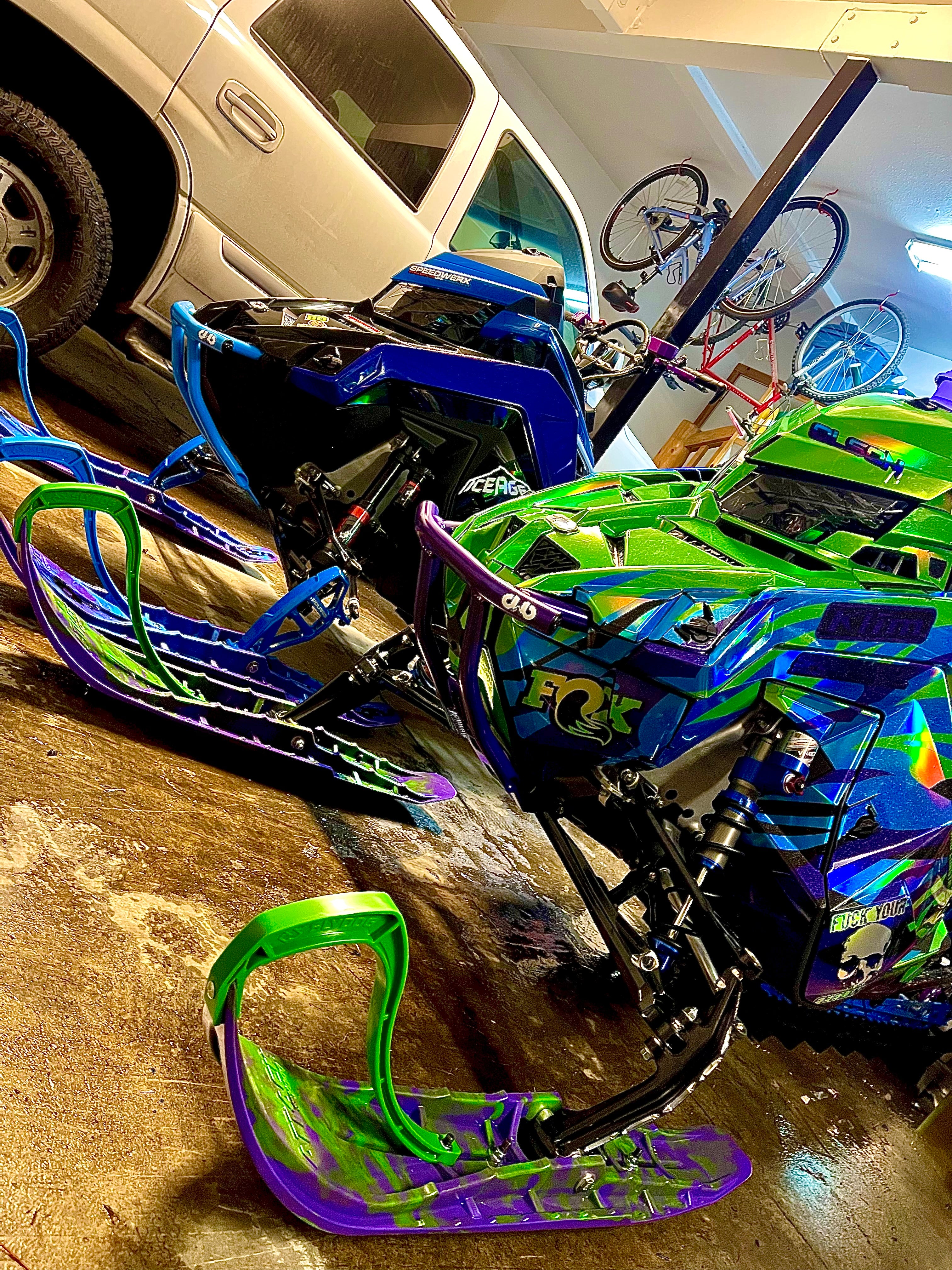 Colorful snowmobiles in a garage with a bicycle in the background