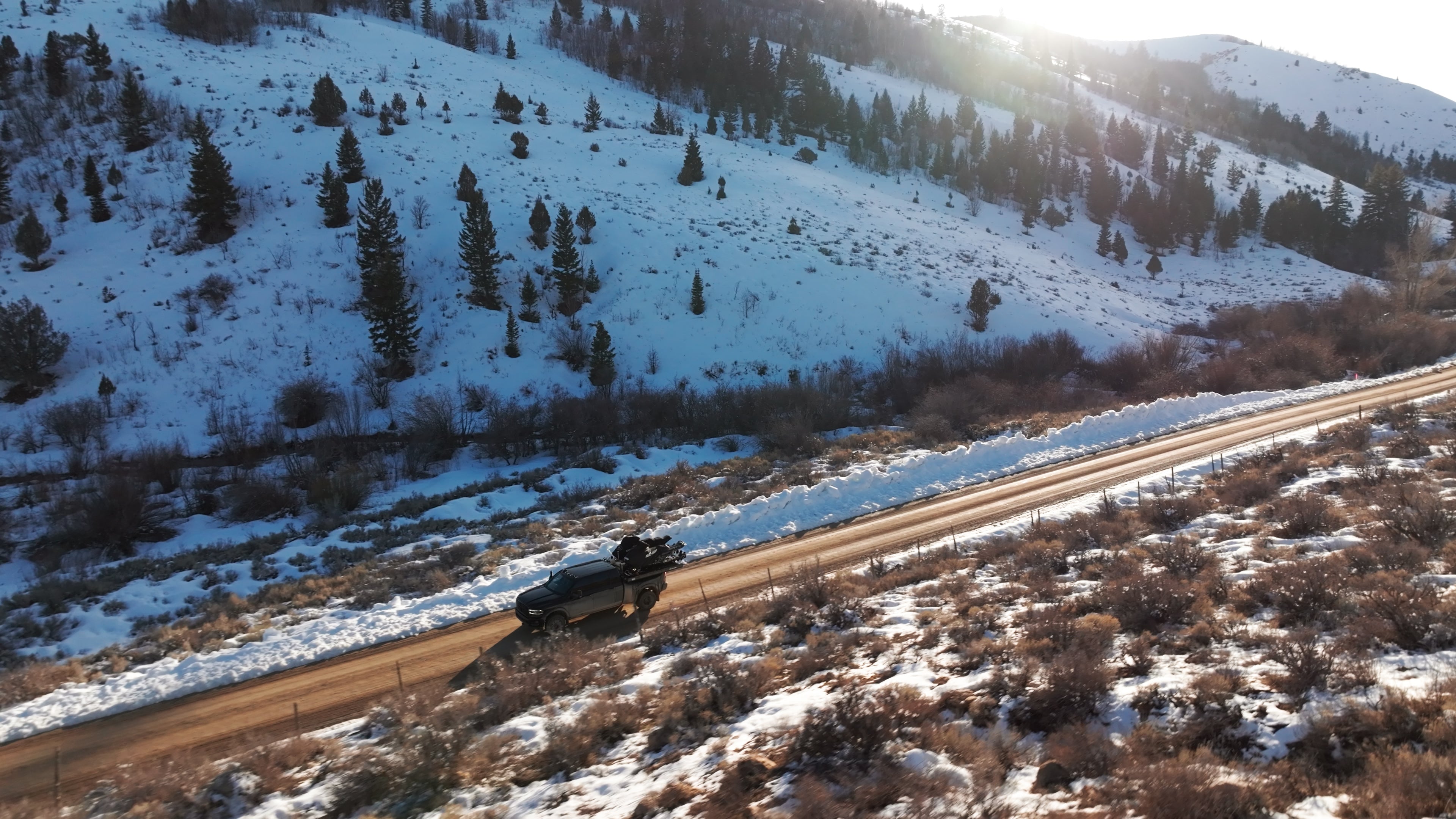Car driving on a snowy mountain road with trees and mountains in the background