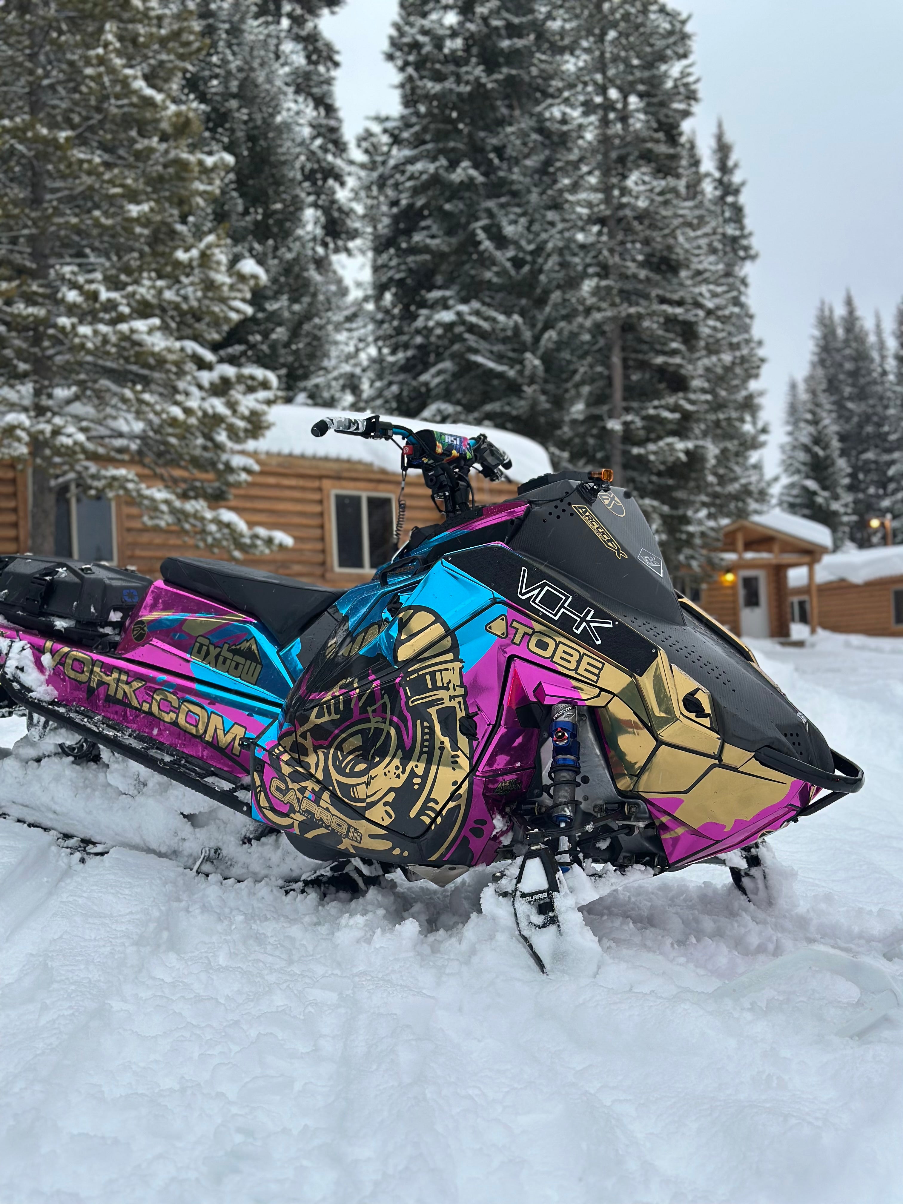Colorful chrome snowmobile in the snow with a wooden cabin and trees in the background