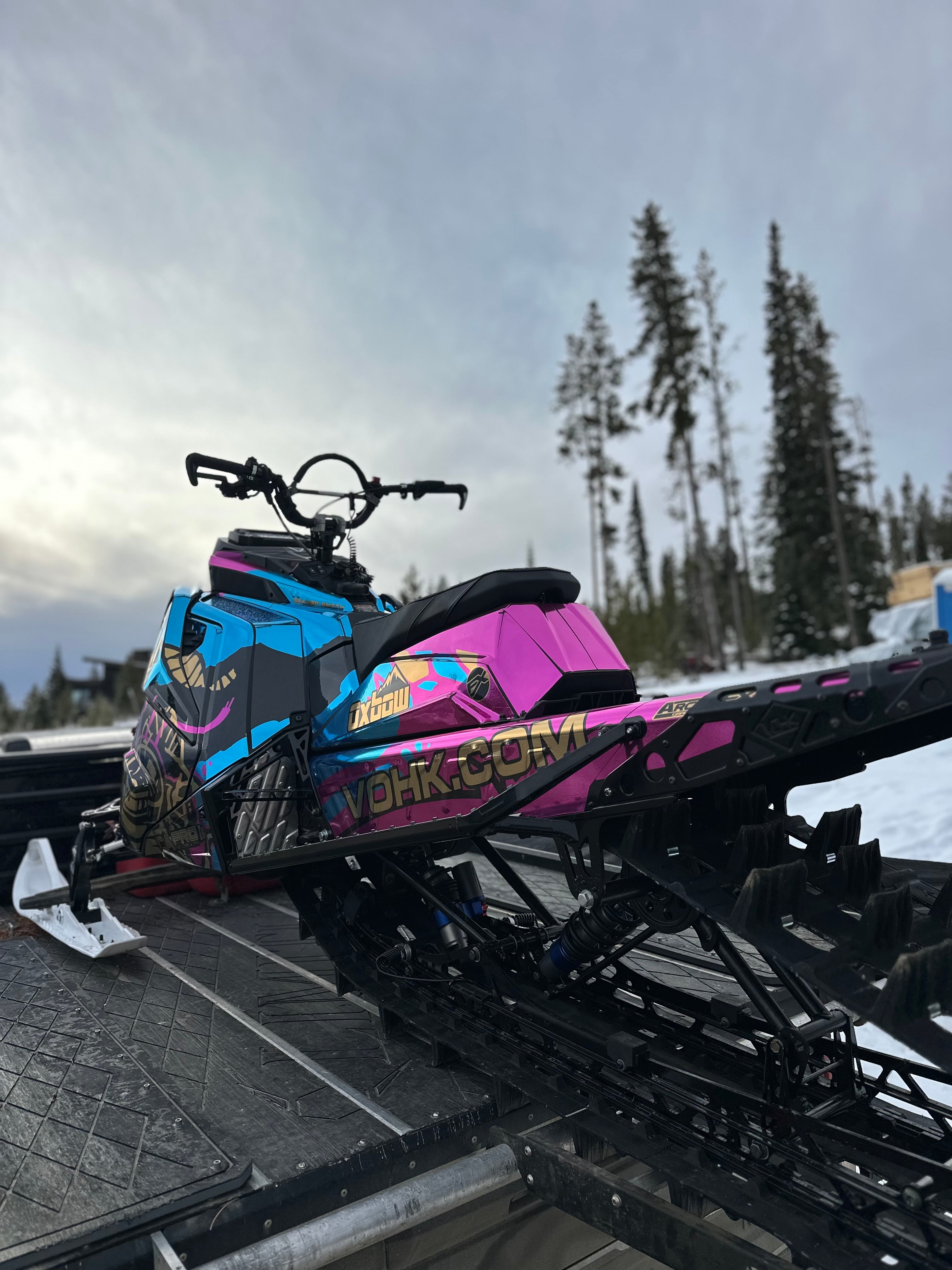 Colorful chrome snowmobile on a trailer with a snowy landscape and trees in the background